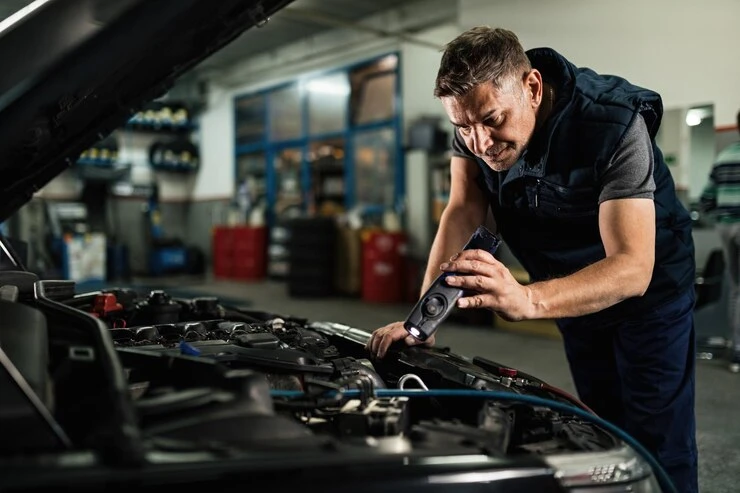 Mecânico inspecionando o motor de um carro, com foco na correia dentada, em um ambiente de oficina automotiva bem equipado.