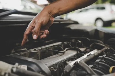 Imagem de um mecânico identificando falhas no motor de arranque. A mão aponta para o motor, sugerindo a importância da manutenção.