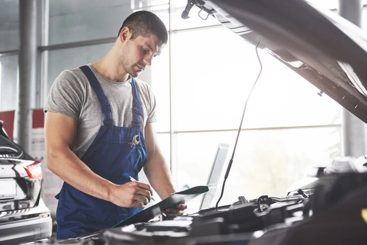 Técnico automotivo inspecionando o motor de um carro enquanto verifica a correia dentada, em um ambiente de oficina.