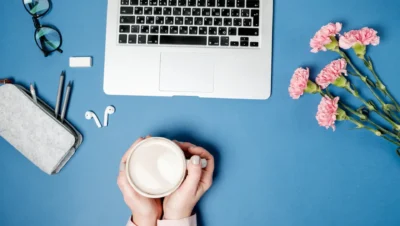 Imagem de uma mesa com laptop, óculos, caneta, fone de ouvido, vela e flores rosas, ideal para criar conteúdo de blog com múltiplos autores e escalar produção.