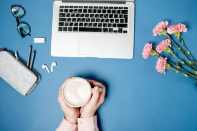 Imagem de uma mesa com laptop, óculos, caneta, fone de ouvido, vela e flores rosas, ideal para criar conteúdo de blog com múltiplos autores e escalar produção.
