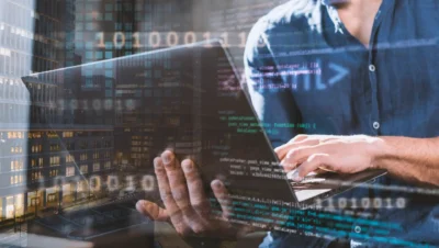 Pessoa usando um laptop com código digital e gráficos sobre computação em borda (Edge Computing), simbolizando tecnologia avançada e processamento de dados próximo ao usuário.