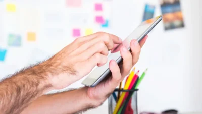 Pessoa planejando conteúdo para redes sociais usando smartphone, com quadro de planejamento e post-its coloridos ao fundo.