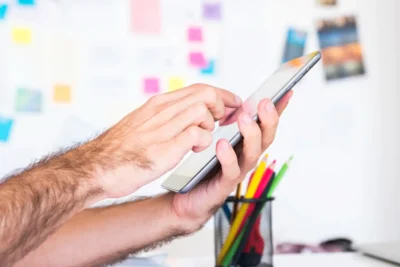 Pessoa planejando conteúdo para redes sociais usando smartphone, com quadro de planejamento e post-its coloridos ao fundo.