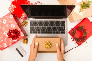 Imagem de uma mesa com presentes de Natal, um laptop e uma pessoa segurando uma caixa presente, ideal para estratégias de Black Friday e Natal em marketing omnichannel.