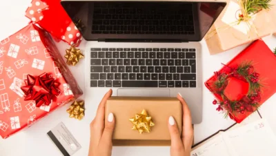 Imagem de uma mesa com presentes de Natal, um laptop e uma pessoa segurando uma caixa presente, ideal para estratégias de Black Friday e Natal em marketing omnichannel.