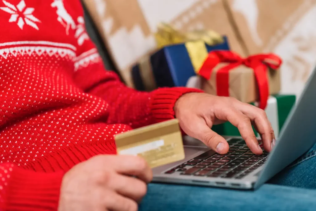 Pessoa fazendo compras online de Natal para aumentar o ticket médio, com presentes ao fundo e usando cartão de crédito.