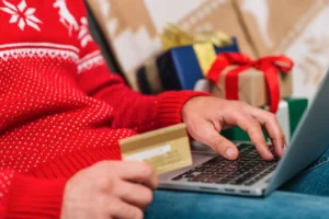 Pessoa fazendo compras online de Natal para aumentar o ticket médio, com presentes ao fundo e usando cartão de crédito.